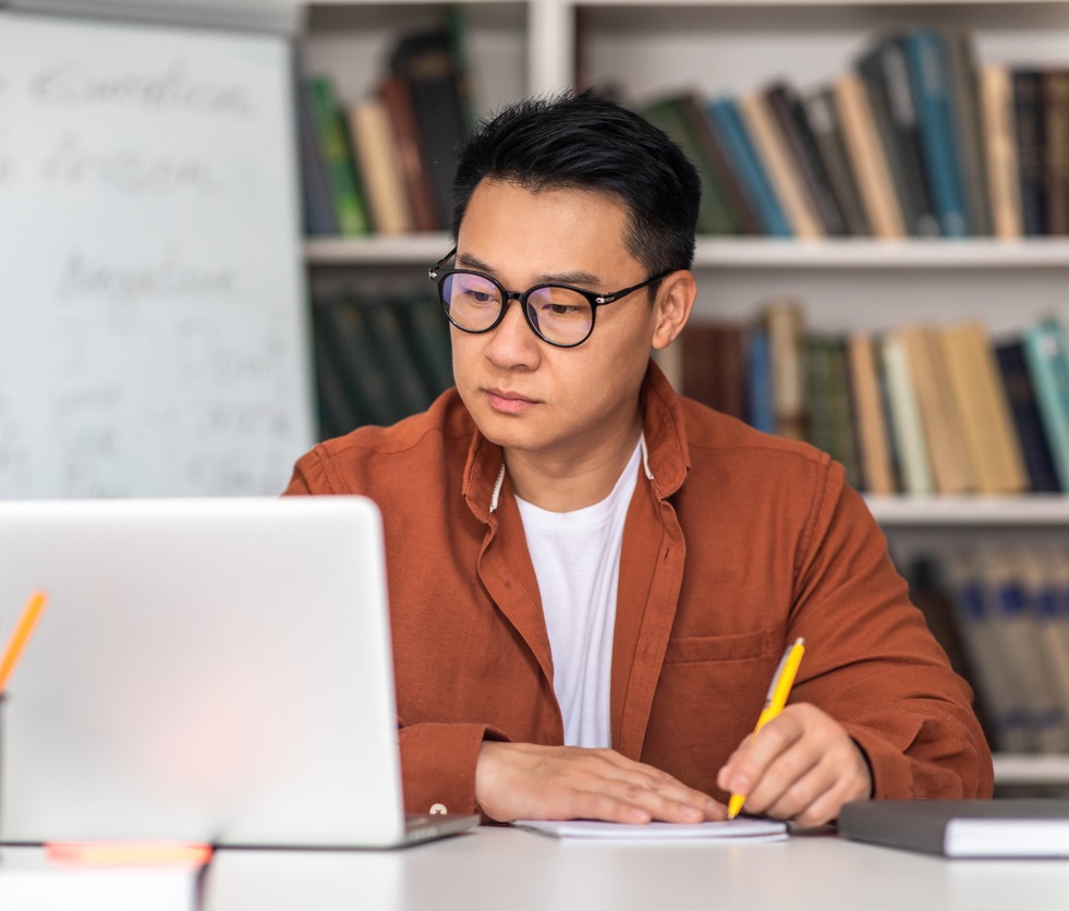 A student in a library taking notes from his laptop