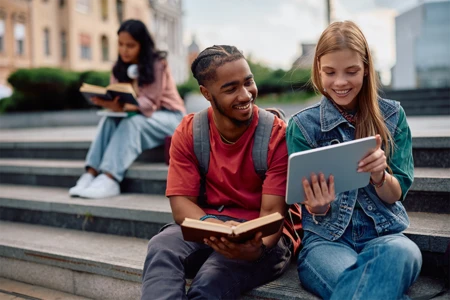 Students sitting on steps looking at a tablet.